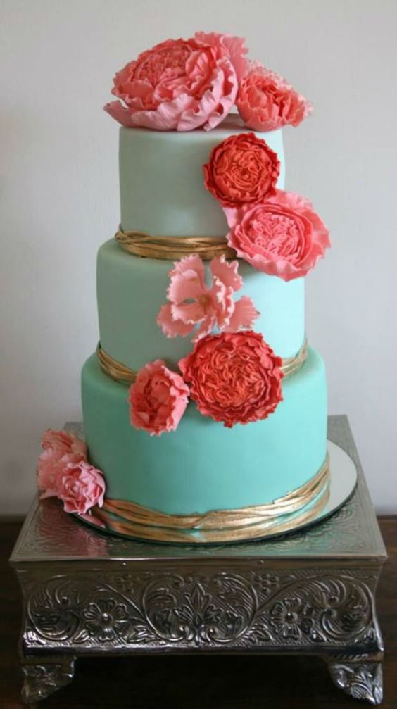 A pink and turquoise Quinceanera cake with three tiers and pink flowers on top