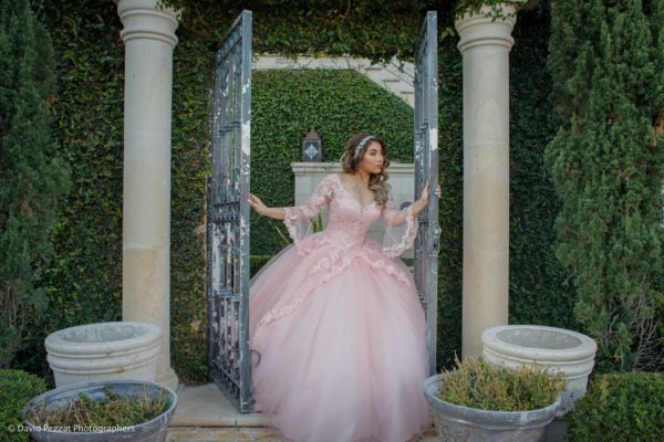A woman in a pink Quinceañera gown standing in a garden