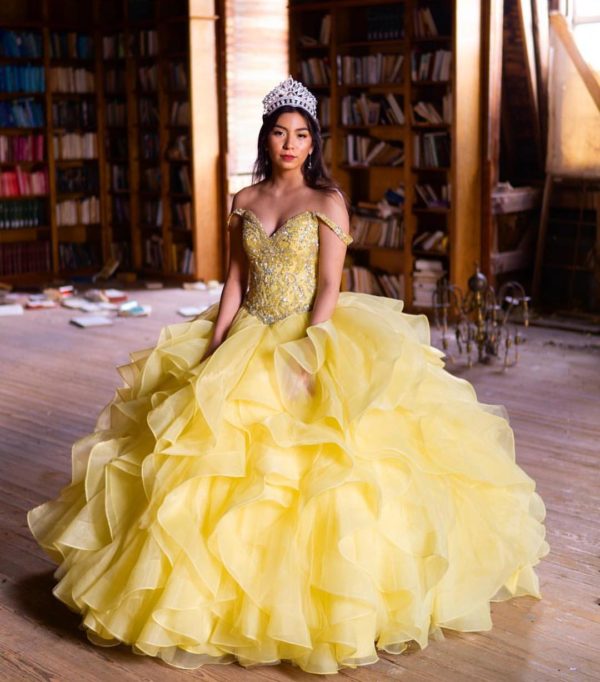 A woman in a yellow Quinceañera dress sitting on a wooden floor