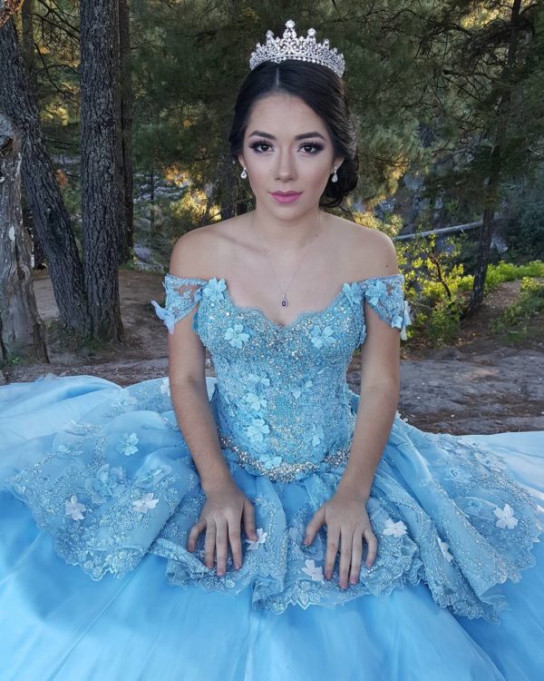 A woman wearing a blue dress and a tiara, with quinceañera makeup