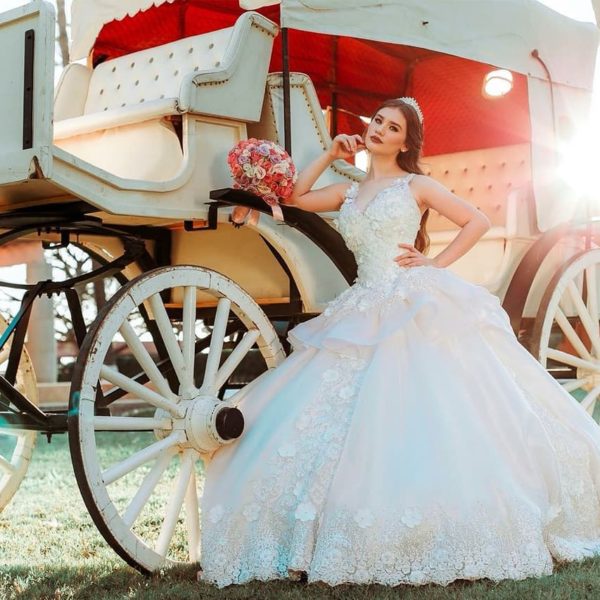 Quinceanera - A woman in a Quinceanera gown sitting in front of a horse drawn carriage