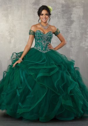 A woman in an emerald green Quinceañera dress posing for a picture in a Quinceanera themed setting.