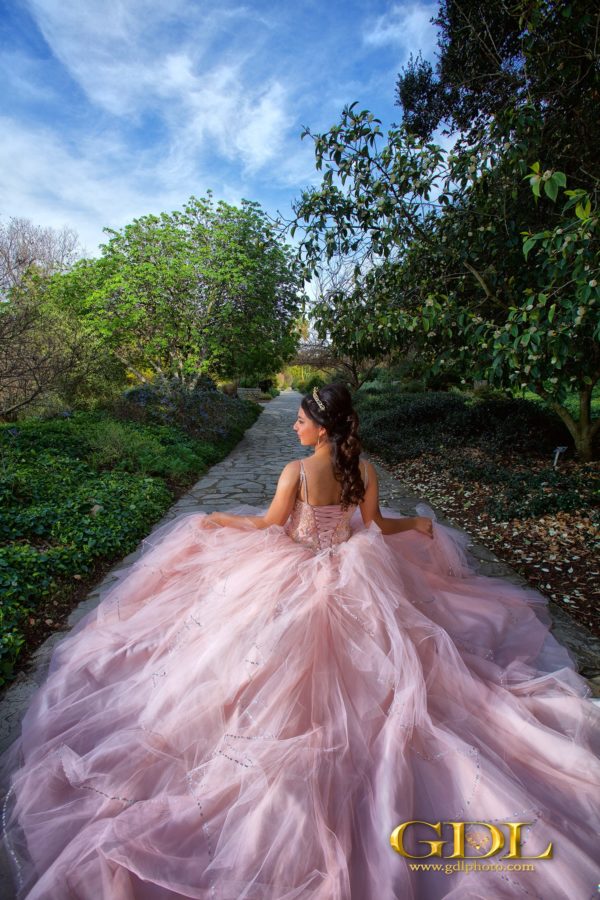 A woman in a pink Quinceanera dress sitting on a path in nature