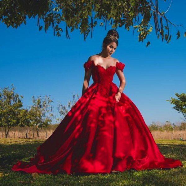 Quinceanera: A woman in a red dress standing under a tree wearing a gown