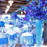 A Quinceañera function hall centerpiece depicting a blue vase with purple flowers on a table.