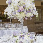 A Quinceanera table decorated with a beautiful lilac floral design, featuring a mix of white and purple flowers.