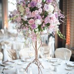 A soft purple Quinceanera theme image featuring a tall vase filled with lots of flowers on top of a table.