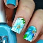 Quinceanera themed nail art: A person holding a blue nail with a flower on it, adorned with blue and green flower nail designs