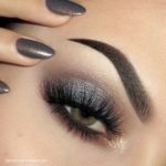 Close up of a woman's eye with a smokey gray eyeshadow and a black manicure for Quinceanera
