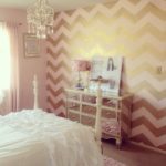 Quinceanera themed pink and gold bedroom with an accent wall, featuring a neatly made bed and a chandelier