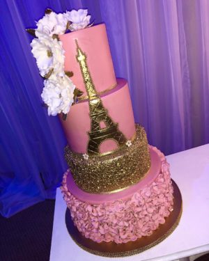 A pink and gold Quinceanera cake decorated with the Eiffel Tower on top