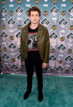 Charlie Puth, a young man standing in front of a green carpet, wearing a Quinceanera outfit