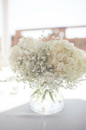 A Quinceanera themed image showing a table centerpiece with a vase filled with white flowers known as baby's-breath