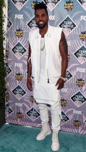 A cool Jason Derulo standing on a blue carpet in front of a wall at a Quinceanera event