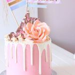 A Quinceanera themed cake with buttercream dripping and a pink color. The cake has a flag on top of it.