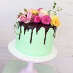 A quinceanera themed cake decorated with sugar, featuring a green cake with chocolate icing and beautiful flowers on top