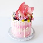 A pink Quinceanera cake with white icing and flowers on top