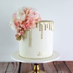 A beautiful Quinceanera cake with white and gold decorations, topped with pink flowers.