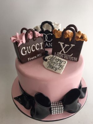 A pastel Gucci birthday cake with black and white decorations, perfect for a Quinceanera celebration.