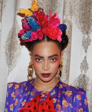 A Quinceanera girl dressed as Frida Kahlo, wearing a colorful dress with a butterfly on her head