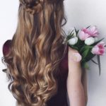 A woman with long curly hair in a down hairstyle, holding a bouquet of flowers at a Quinceanera event.