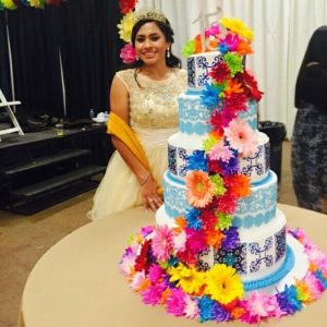 Quinceanera dresses, a woman standing in front of a cake with flowers on it, quinceanera mexican cakes