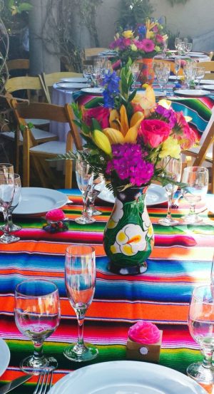Quinceañera dresses and a colorful table setting with flowers in a vase, creating a Mexican themed Quinceañera atmosphere.