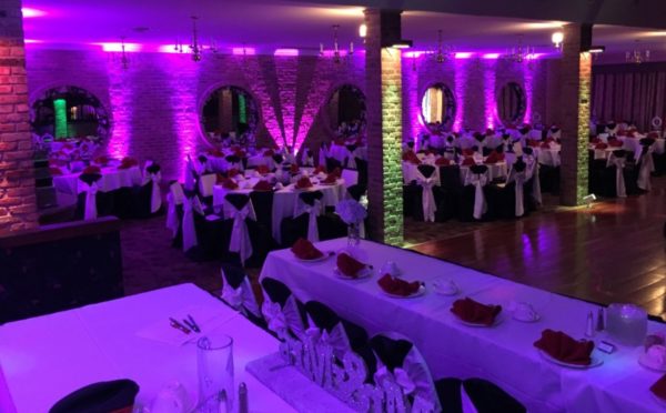 Quinceanera reception in a spacious function hall with tables and chairs, illuminated with purple lighting.