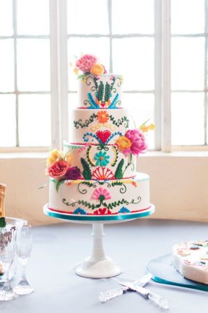 A Mexican themed Quinceanera cake, featuring a charro design and vibrant flowers, displayed on a table.