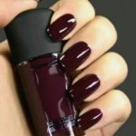 A person holding a bottle of dark wine nail polish