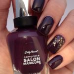 A person holding a bottle of plum color nail polish