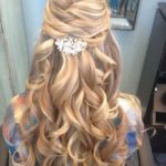 A woman with long blonde hair and a flower in her hair, showcasing a formal half up half down hairstyle for Quinceanera.