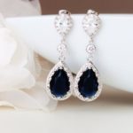 A pair of Quinceanera earrings, featuring sapphire and diamond, placed on a white plate.