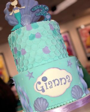 A Sugar cake decorated with blue and purple colors featuring a little mermaid on top for a Quinceanera celebration