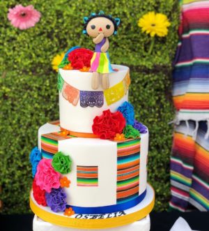 A colorful Quinceañera cake with a doll on top, following a Mexican theme