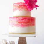 Quinceanera themed image of a three-tiered watercolor cake, adorned with pinks and gold. The cake features a pink flower on top.