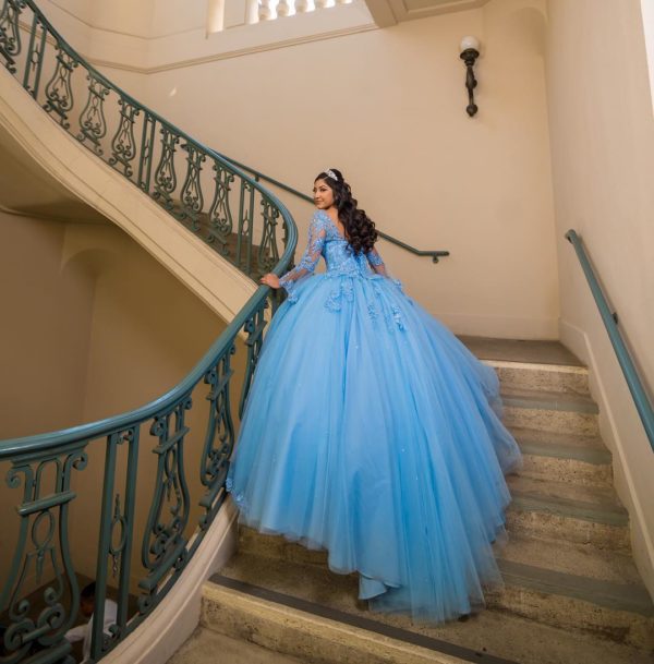 A woman in a blue dress is standing on a set of stairs wearing Emily's dream Quinceanera dress.
