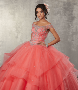 A woman posing for a picture in a red Quinceañera dress among coral Quinceañera dresses