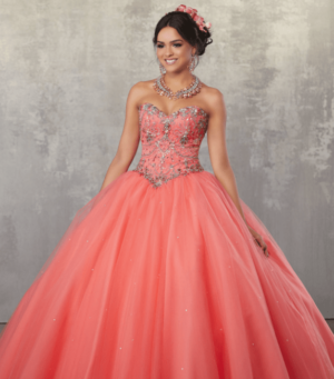 A woman in a coral Quinceañera dress creation, posing for a picture in a ball gown