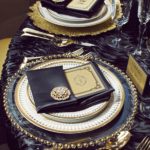 A metal table set with a black and gold place setting, perfect for a Quinceanera celebration