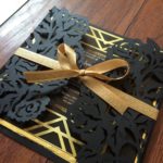 A close up of a black and gold Quinceanera invitation made of wood