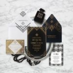 A black and gold Quinceanera invitation suite displayed on a marble table