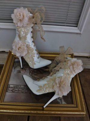 A pair of white high heeled shoes sitting on top of a picture frame, representing a Victorian Quinceanera theme.