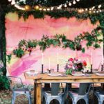 A beautiful quinceanera setup with a floral design, featuring a wooden table and silver chairs against a pink wall.
