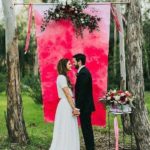A Quinceanera photograph of a bride and groom standing in front of a red backdrop