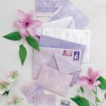 A beautifully arranged Quinceanera invitation featuring cut flowers on a white table, adorned with numerous purple envelopes.