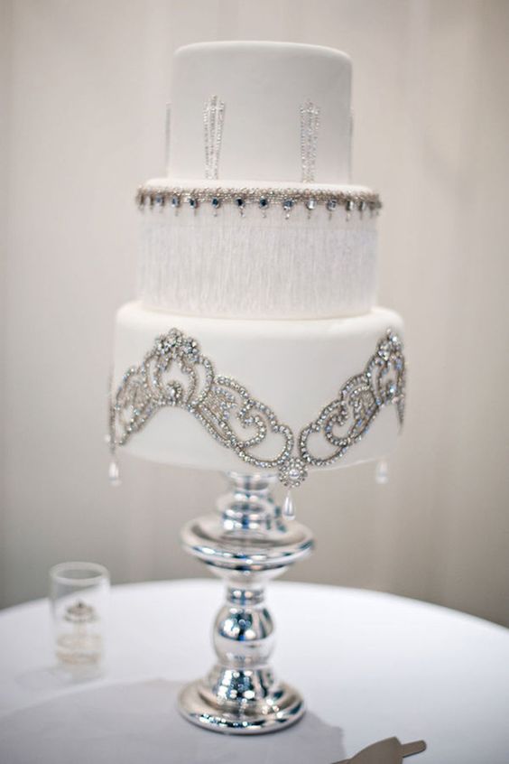 A white Quinceanera cake with silver decorations on a table