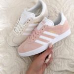 A person holding a pair of pink and white adidas Originals Gazelle walking shoes for a Quinceanera event.