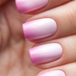 A Quinceanera-themed image featuring a woman's hand with light to dark ombre nails, showcasing a beautiful pink and white manicure design.