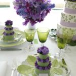 A Quinceanera invitation featuring lilac colors, set on a table with a cake and decorated with purple flowers.